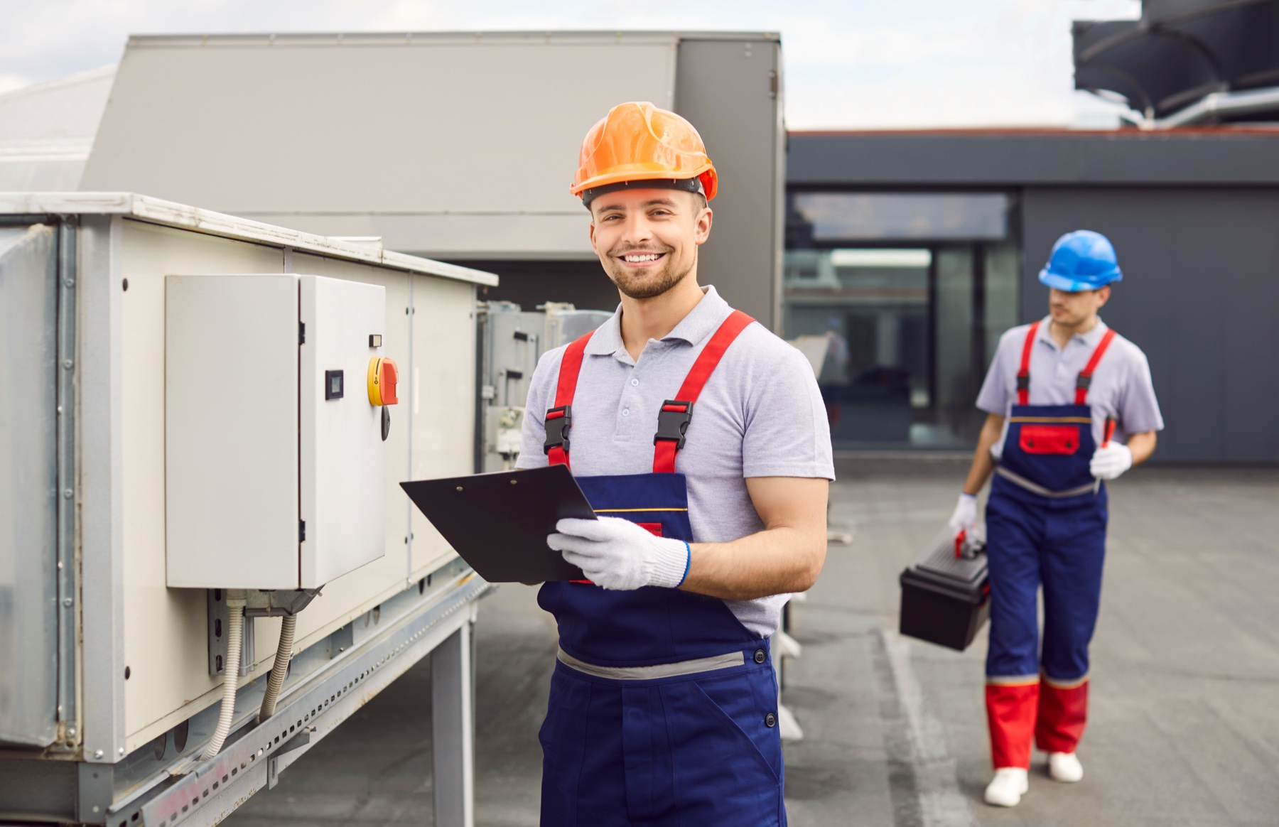 Canyon Plumbing & Heating technician with a clipboard beside a rooftop HVAC unit